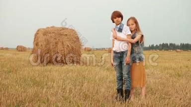 年轻夫妇在干草堆背景下的收获场上拥抱。 拥抱在农村摆姿势的少年女孩和男孩